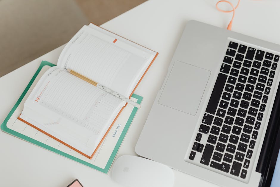 Top view of a clean workspace with a laptop, notebook, and mouse on a desk.